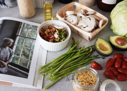 A selection of fresh vegetables and a cookbook in a kitchen setting, promoting healthy cooking.