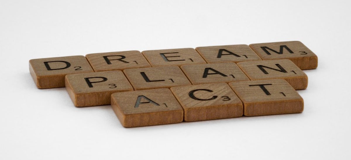 Wooden Scrabble tiles forming the motivational words: Dream, Plan, Act on white background.
