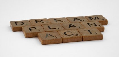 Wooden Scrabble tiles forming the motivational words: Dream, Plan, Act on white background.