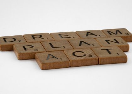 Wooden Scrabble tiles forming the motivational words: Dream, Plan, Act on white background.