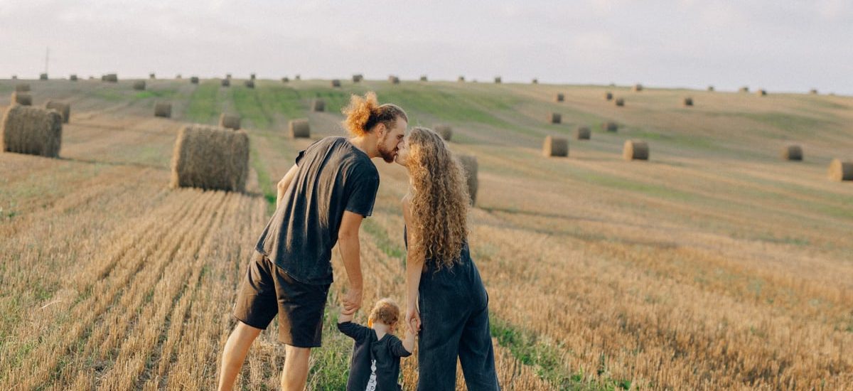 A couple with their child enjoy a sunny day in a wheat field, symbolizing love and joy.