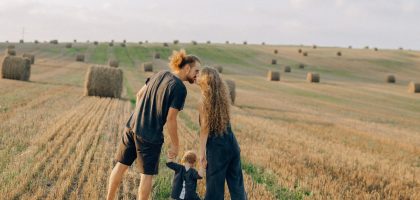 A couple with their child enjoy a sunny day in a wheat field, symbolizing love and joy.