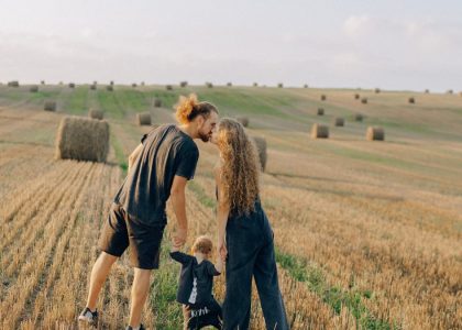 A couple with their child enjoy a sunny day in a wheat field, symbolizing love and joy.